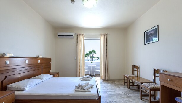 A hotel room with a bed, a desk, a chair, a small table, and a view of the beach. - Mammis Beach (Kos)