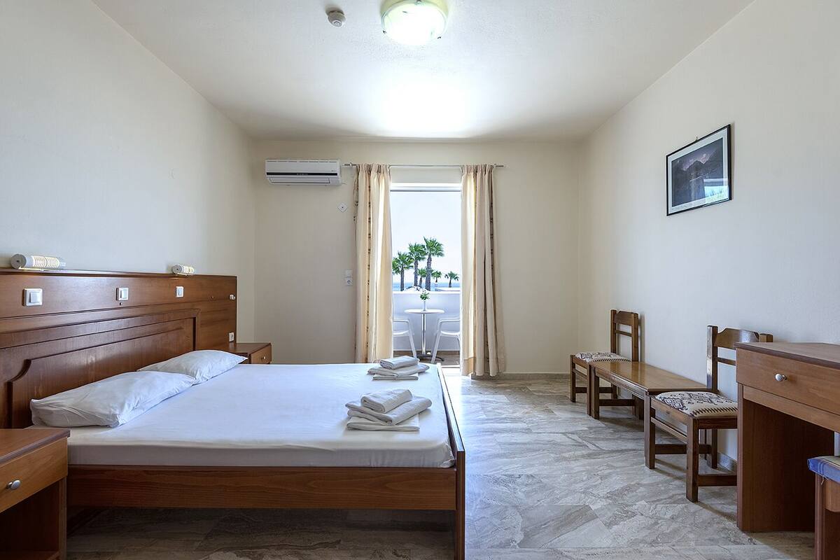 A hotel room with a bed, a desk, a chair, a small table, and a view of the beach.