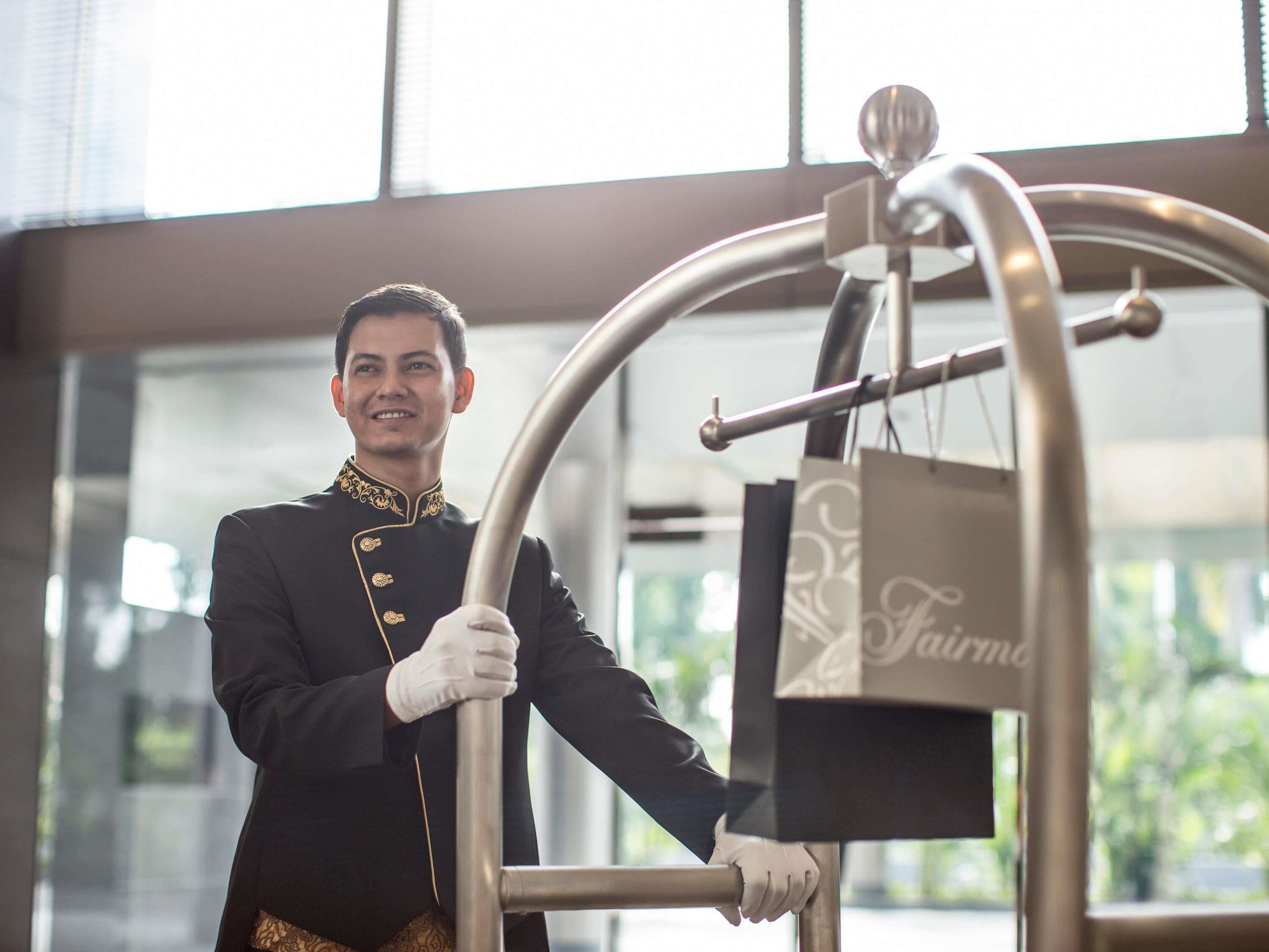 Una persona con uniforme empujando un carrito de equipaje en un moderno vestíbulo de hotel con ventanas amplias.