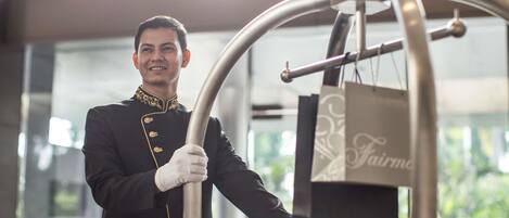Una persona con uniforme empujando un carrito de equipaje en un moderno vestíbulo de hotel con ventanas amplias.