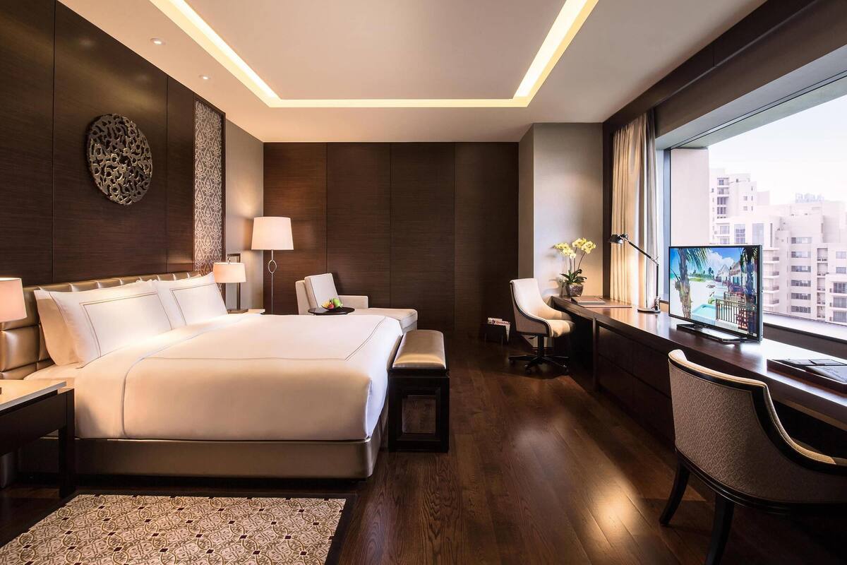 A modern hotel room with a large bed, a desk, a chair, and a TV.