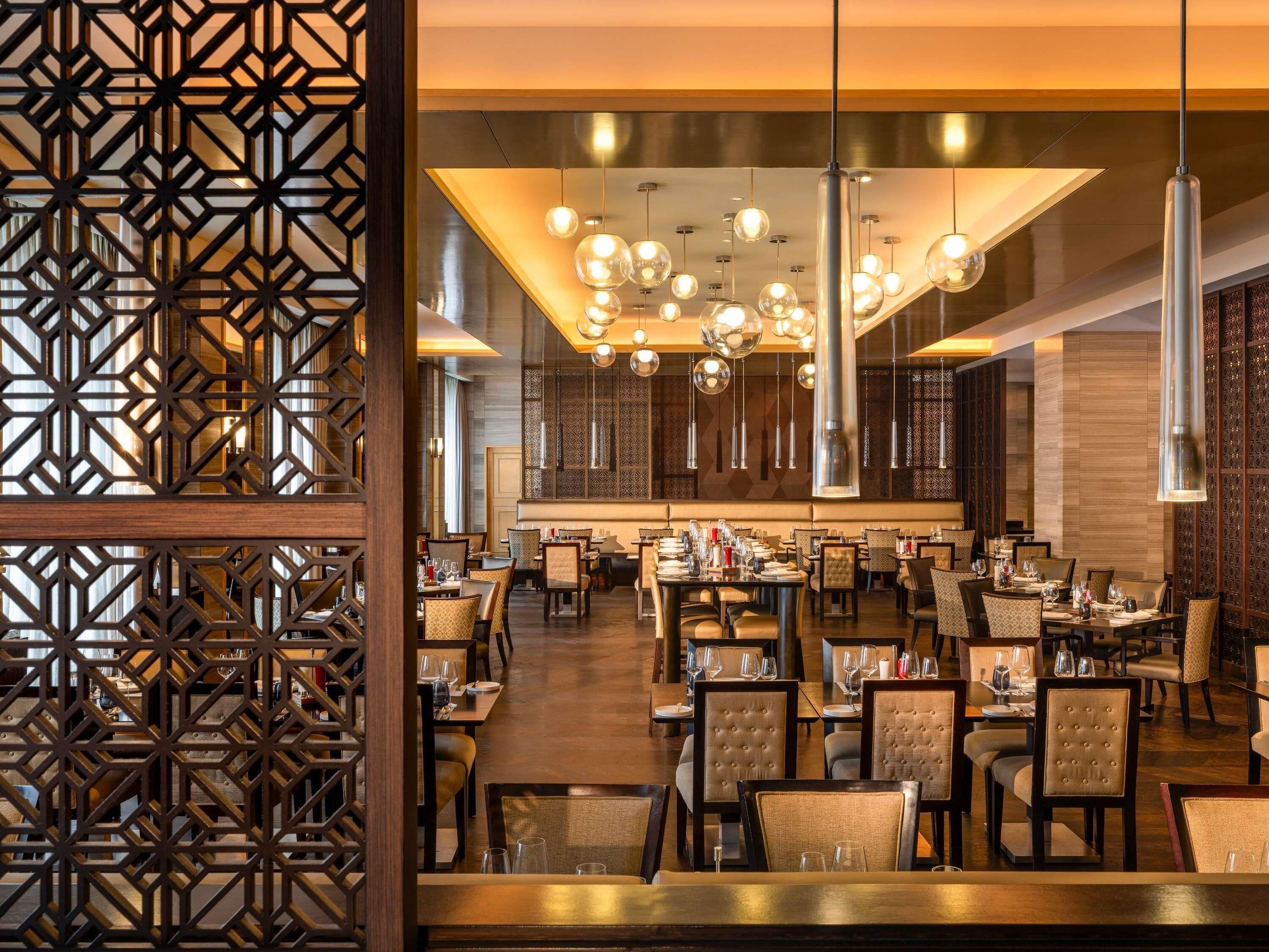 Un restaurante espacioso con varias mesas, iluminación colgante moderna y un panel de madera decorativo.
