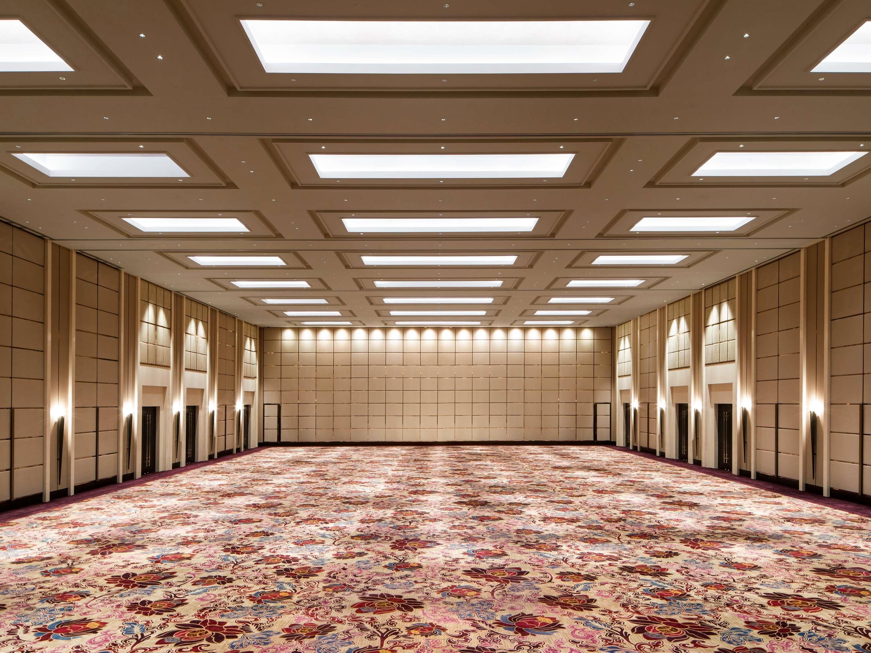 A large, well-lit room with a patterned carpet, recessed lighting, and a high ceiling with skylights.
