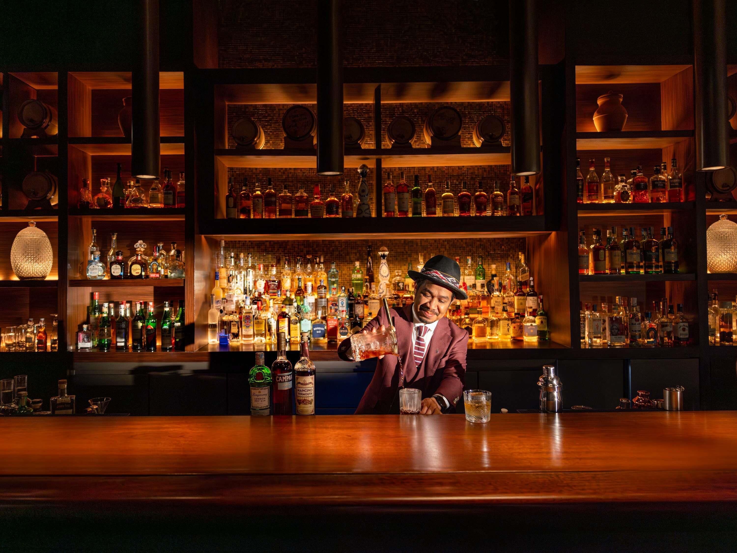 Un bar con estantes llenos de botellas de licor, un cantinero y una barra de madera.