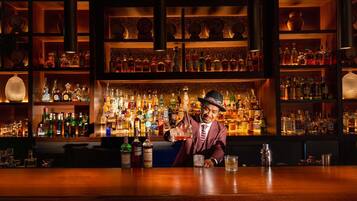 Un bar con estantes llenos de botellas de licor, un cantinero y una barra de madera.