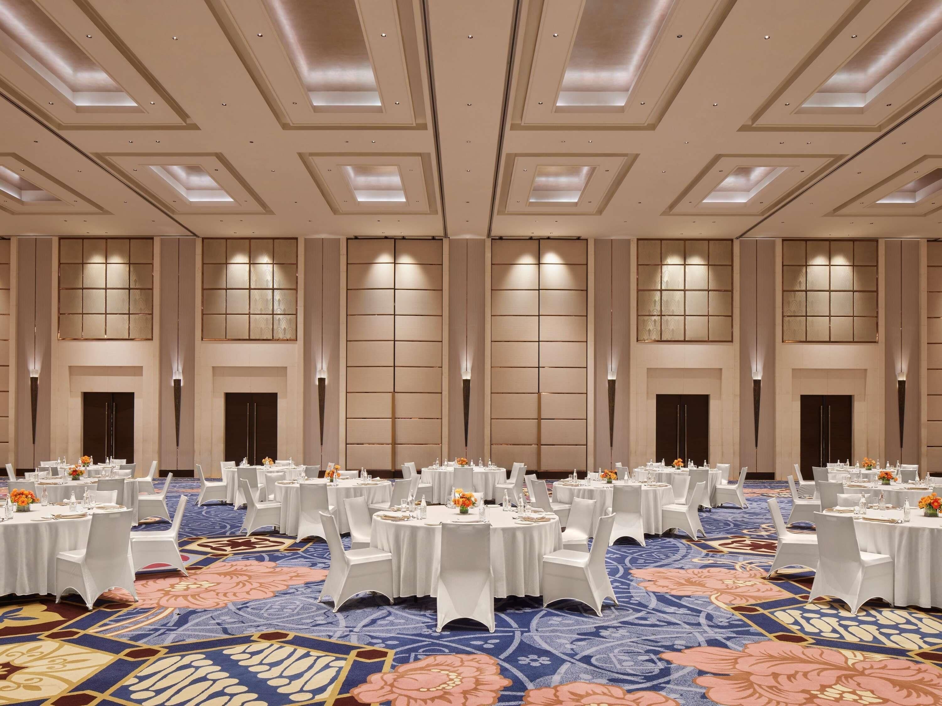 A large banquet hall with multiple round tables, white chairs, and a patterned carpet.