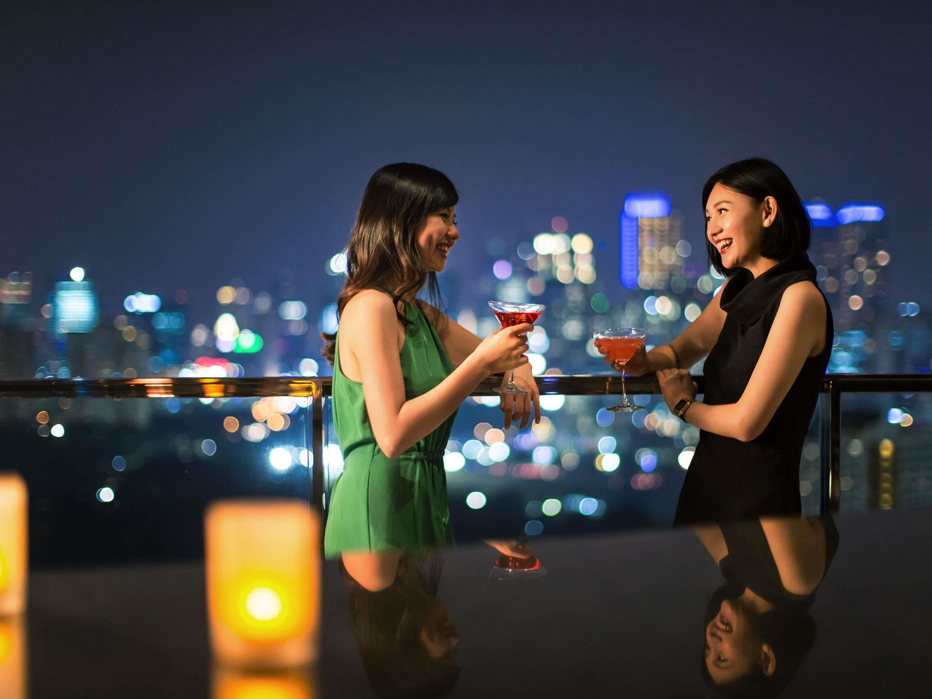Two people at a bar with a city skyline in the background.