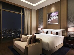 A modern hotel room with a large bed, a sofa, a city view, and a nightstand with a lamp. - Fairmont Jakarta (Jakarta)