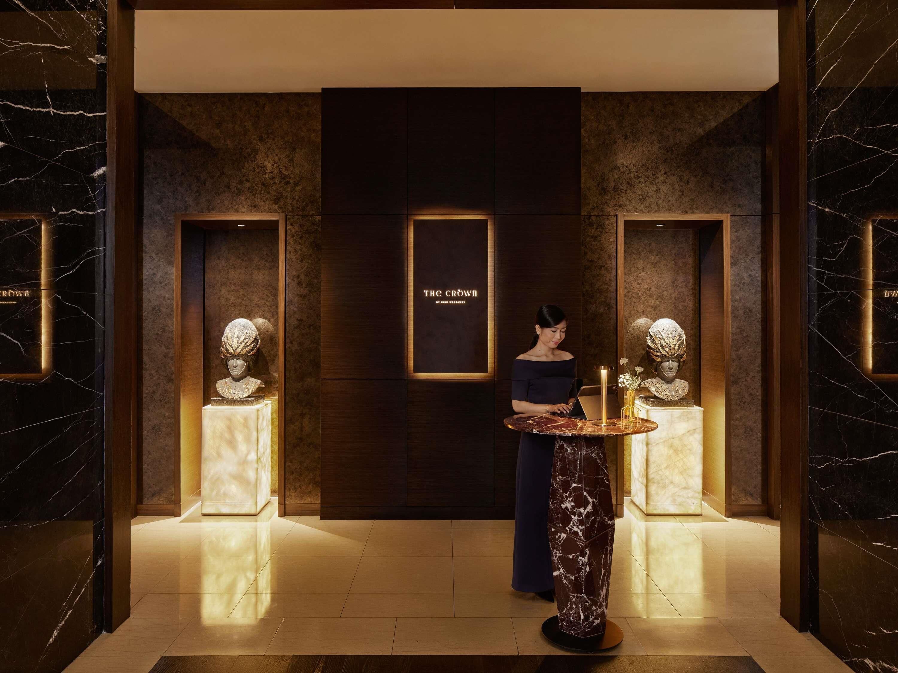 A lobby with a marble floor, a reception desk, and two illuminated bust sculptures.