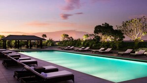 Zona de piscina con sillones de descanso y un espacio de estar cubierto durante el atardecer.