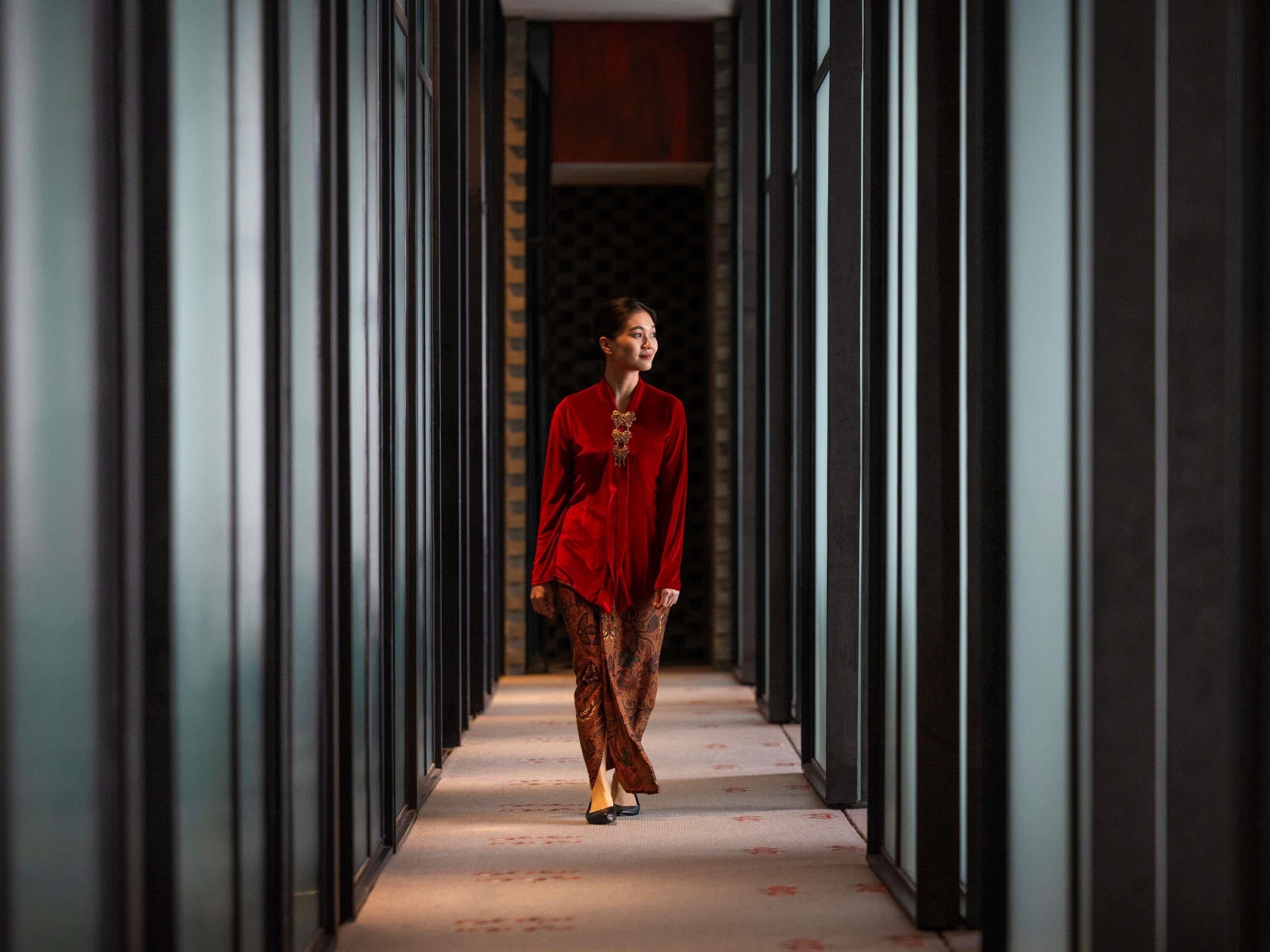 A person walking down a hallway with a patterned floor and dark walls.