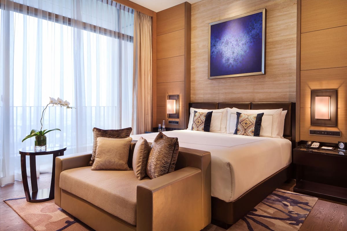 A hotel room with a large bed, a sofa, a small table with a plant, and a wall-mounted painting.