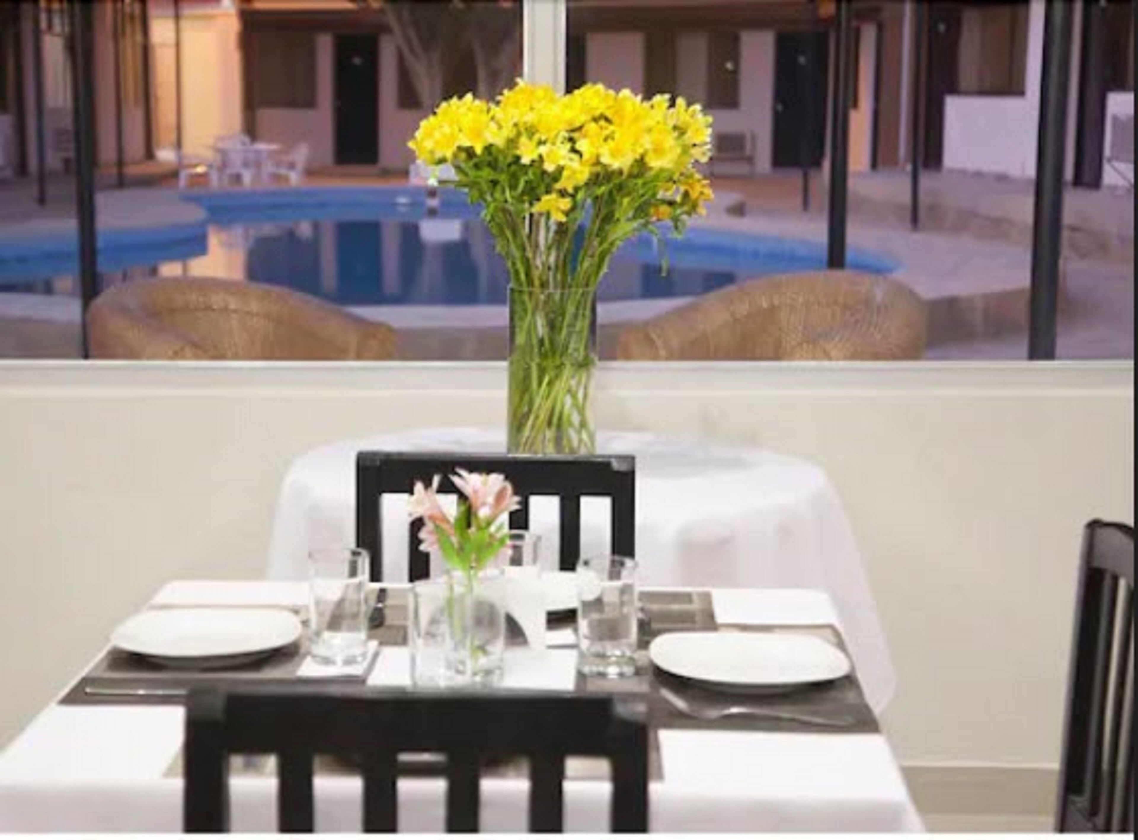 A dining table set for two with a vase of yellow flowers, a glass of water, and a menu.