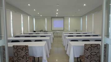 Une salle de conférence équipée de plusieurs tables et chaises, d’un écran de projection et d’un présentoir à l’avant.