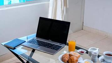 Um laptop sobre uma mesa de vidro com itens de café da manhã, vista para a piscina e o texto 'TRABAJA SEGURO' na parte superior.