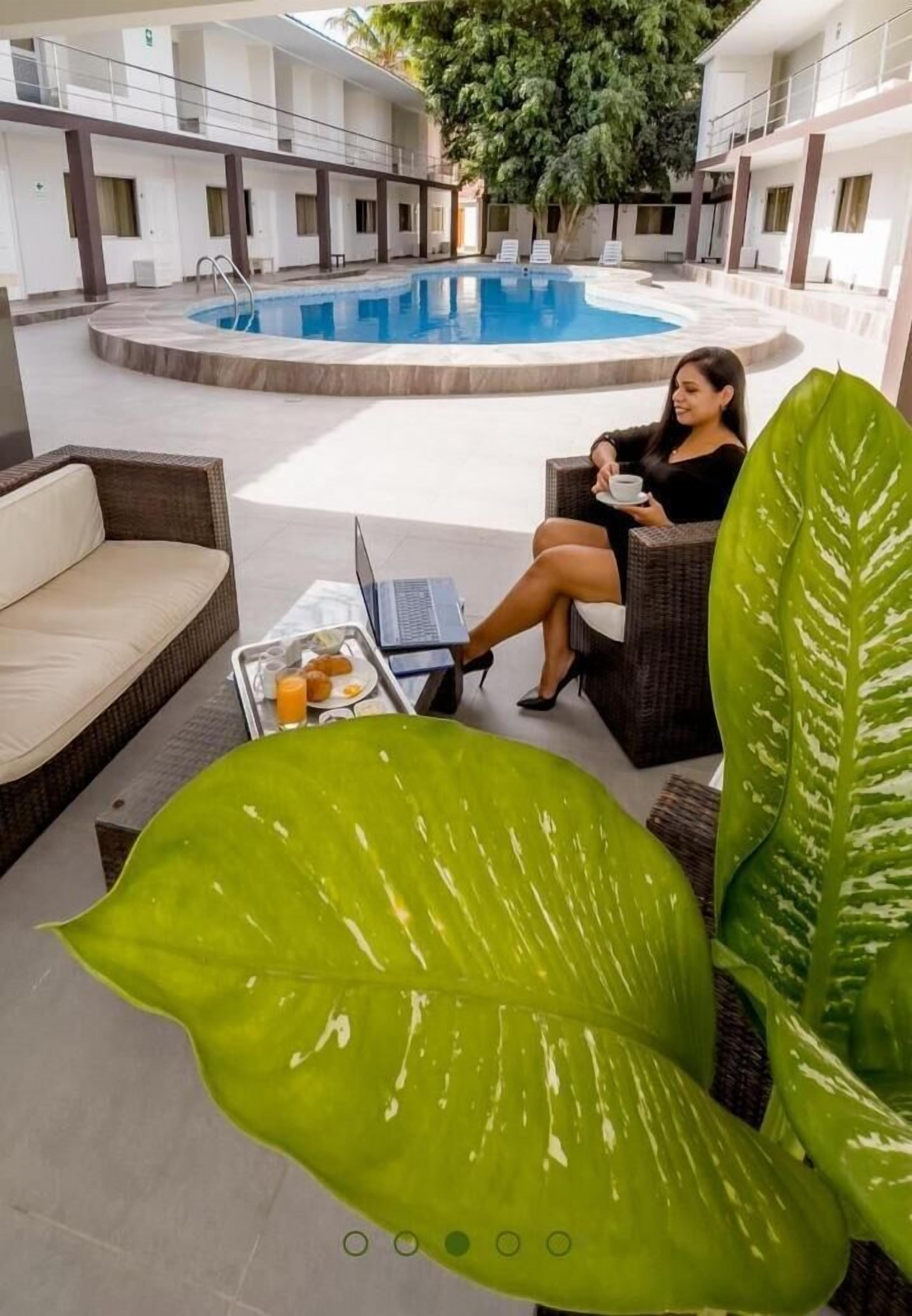 Un espace aménagé au bord de la piscine, avec un fauteuil de relaxation, une table à manger sur laquelle se trouve un plateau de nourriture et de boissons, et une grande plante verte.