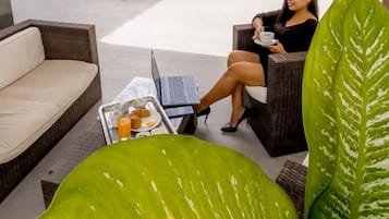Un espace aménagé au bord de la piscine, avec un fauteuil de relaxation, une table à manger sur laquelle se trouve un plateau de nourriture et de boissons, et une grande plante verte.