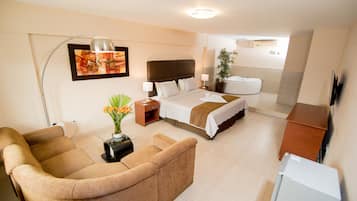 A hotel room with a bed, a sofa, a desk, a lamp, a plant, and a TV.