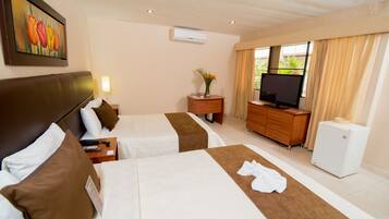A hotel room with two beds, a TV, a small refrigerator, a nightstand, a lamp, and a painting of tulips on the wall.
