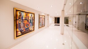 A corridor with two large framed artworks on the walls, a polished white floor, and glass doors leading to another area. - El Angolo Hotel Piura (Piura)