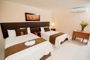 Habitación de hotel con dos camas, un escritorio, una silla, una mesita de noche, una lámpara y un cuadro en la pared.