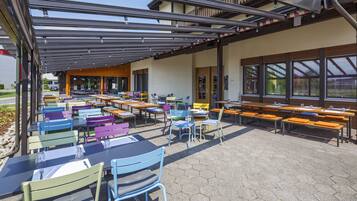 An outdoor dining area with multiple tables and chairs, a covered seating area, and large windows.