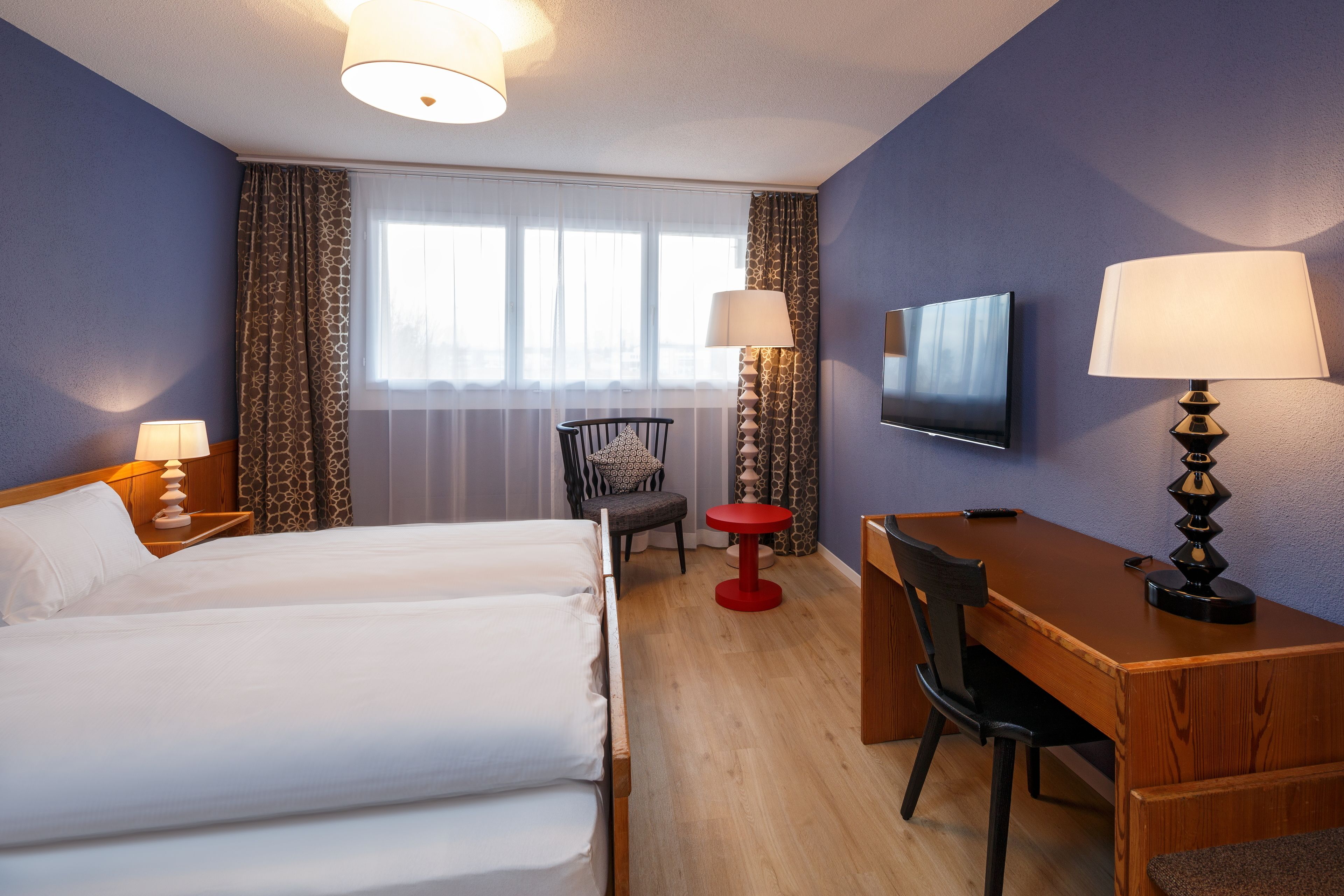 Ein Hotelzimmer mit einem Bett, einem Schreibtisch, einem Stuhl, einem Fernseher und einem fenster mit Vorhängen.