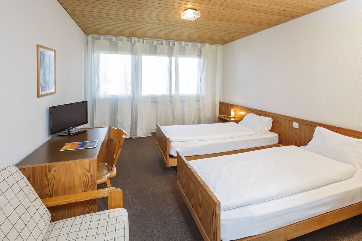 Een hotelkamer met twee eenpersoonsbedden, een houten bureau met stoel, een televisie en een raam met gordijnen.