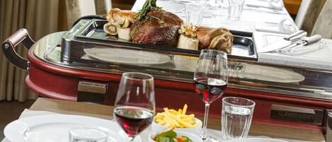 A dining table set with plates, glasses, and a glass of red wine.