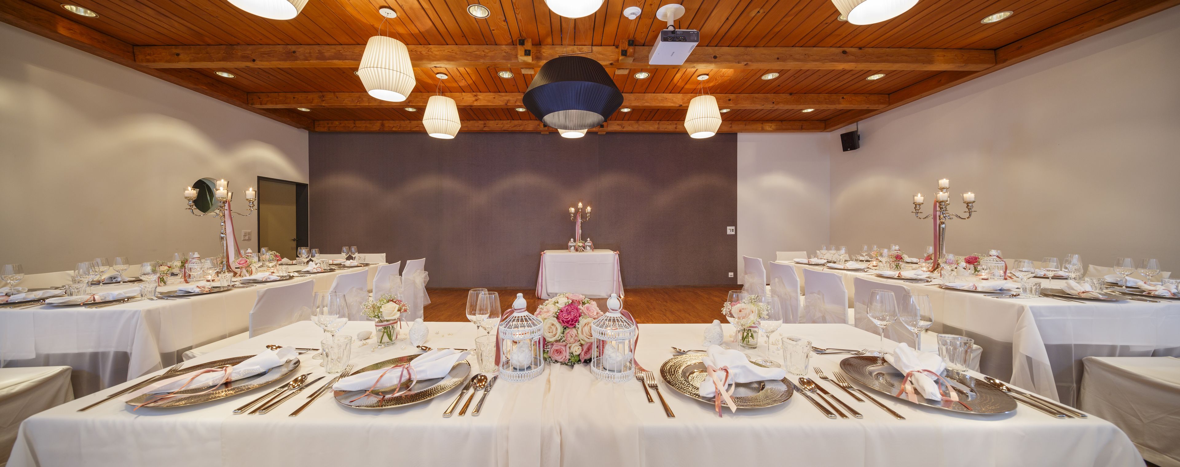 A banquet hall with tables set for a formal event, featuring white tablecloths, silverware, and floral centerpieces.