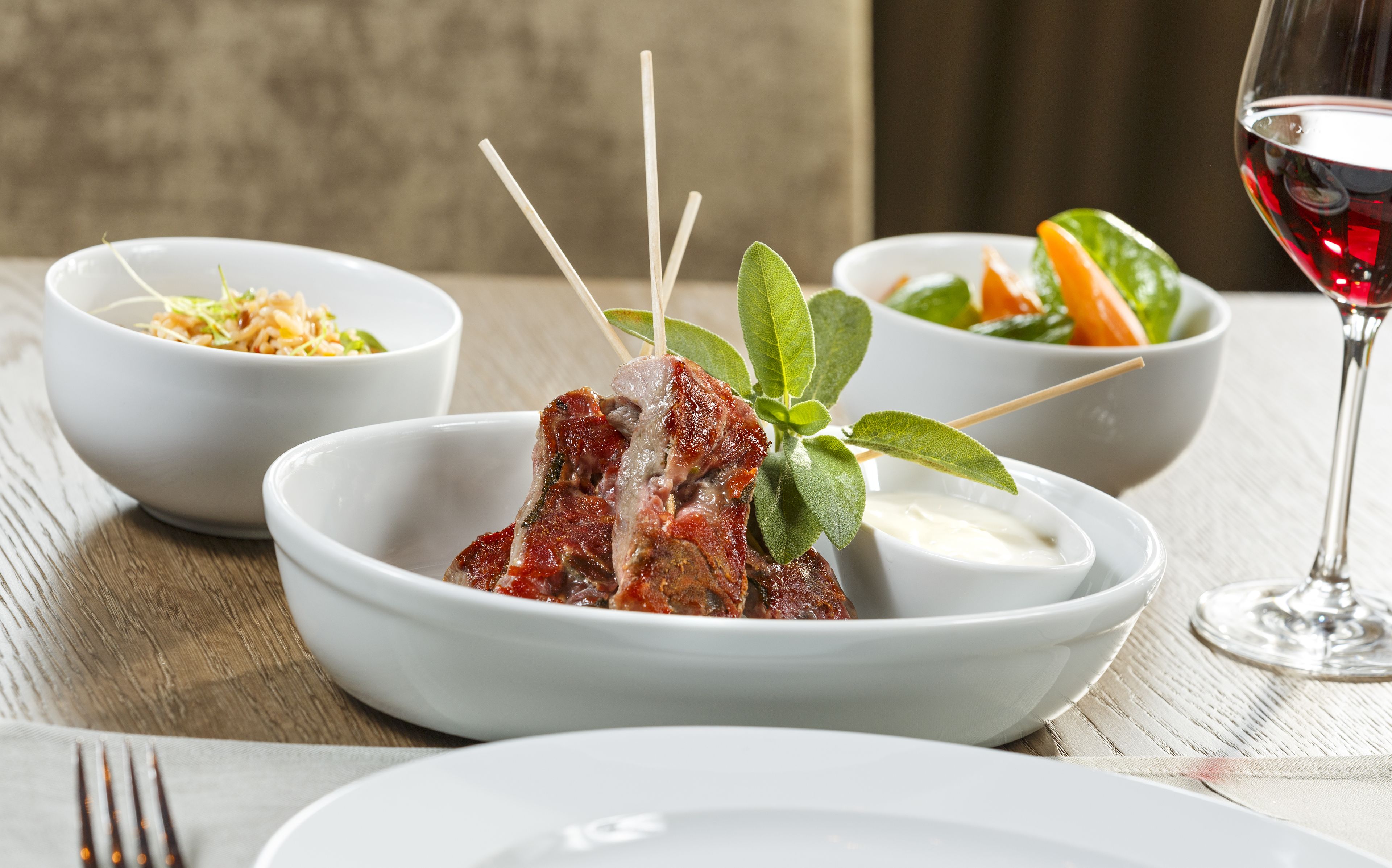 A dining table with white bowls containing food, a glass of red wine, and a fork.
