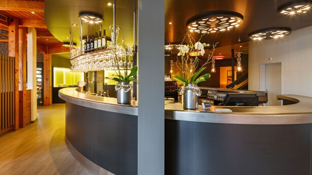 A modern reception area with a curved counter, potted plants, and a bar stocked with bottles. - CHÄRNSMATT Gasthof & Spielparadies (Rothenburg)