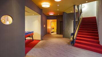 Un interior moderno con una escalera alfombrada de color rojo, una mesa de fútbol de mesa y un pasillo que conduce a una habitación luminosa.