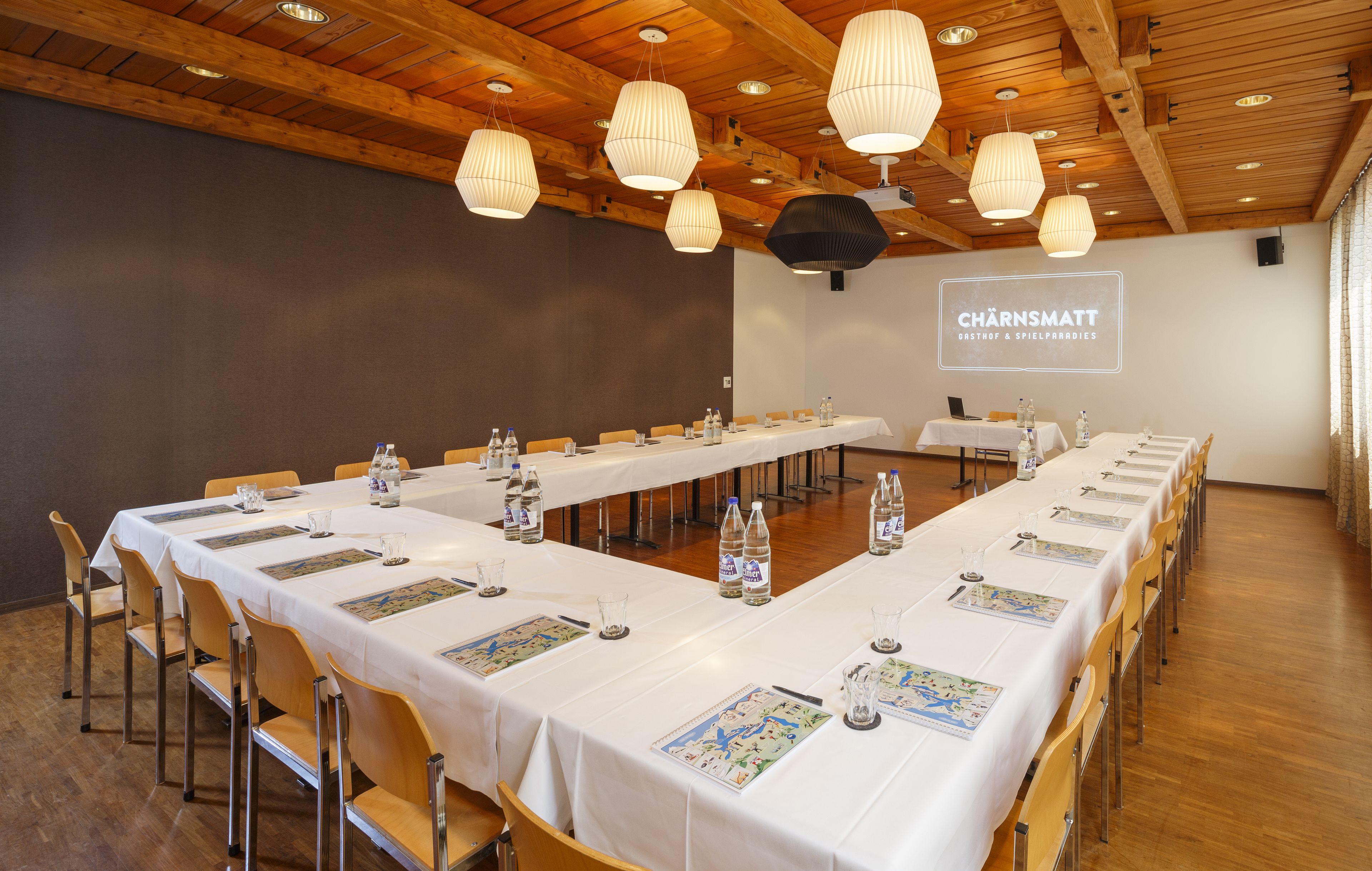 Ein Konferenzraum mit langen Tischen, Stühlen und hängenden Lampen.