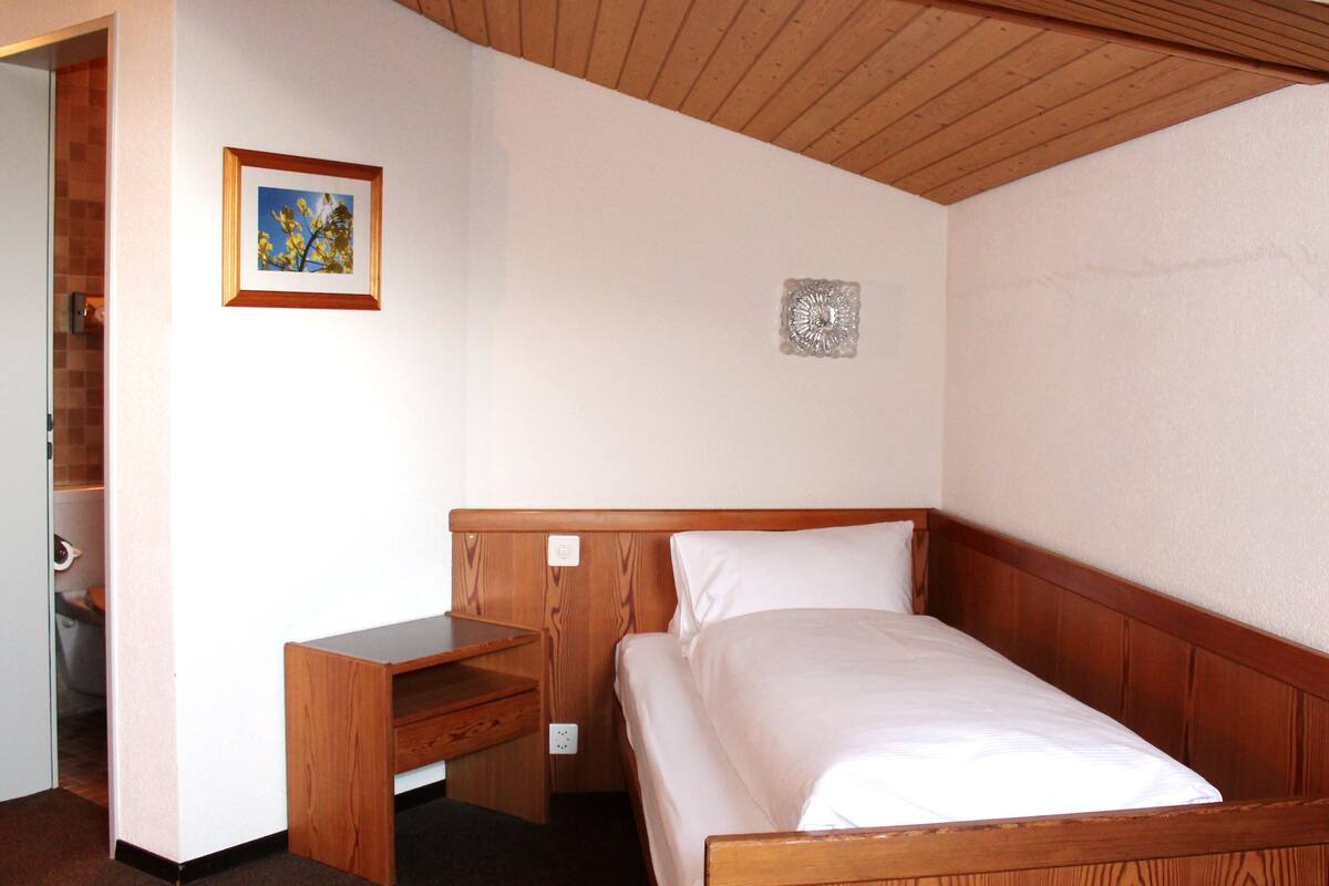 Een slaapkamer met een houten bed, een nachtkastje, een klein bureau en een lijst met een afbeelding aan de muur.