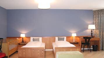 A room with two wooden beds, a desk, a chair, a small table, a lamp, and a trash bin.