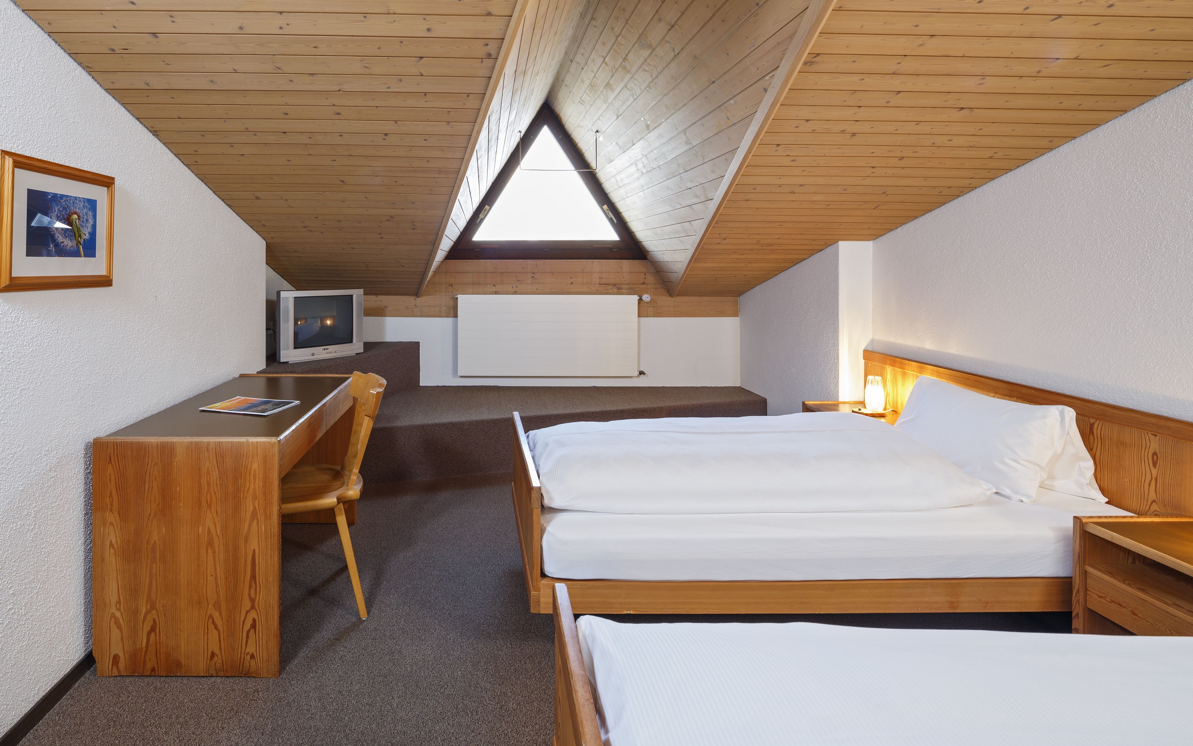 A room with a sloped ceiling, wooden furniture, a bed, a desk, and a television.