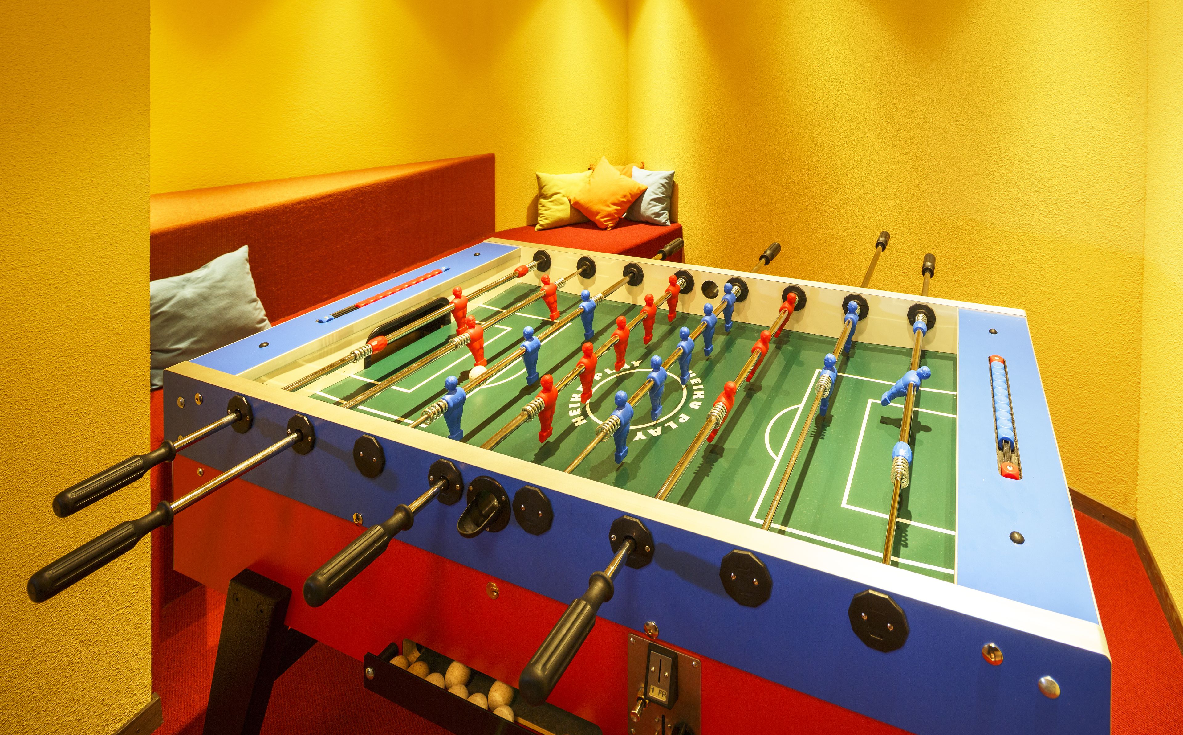 A foosball table in a room with yellow walls and a red couch.