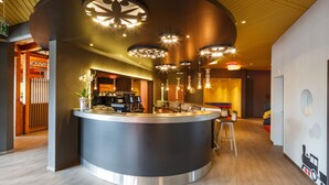 A modern hotel lobby with a central bar area, wooden flooring, and contemporary lighting fixtures. - CHÄRNSMATT Gasthof & Spielparadies (Rothenburg)