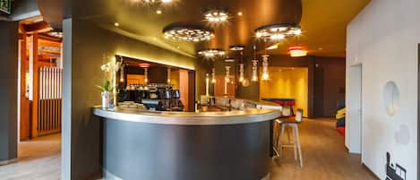 A modern hotel lobby with a central bar area, wooden flooring, and contemporary lighting fixtures.