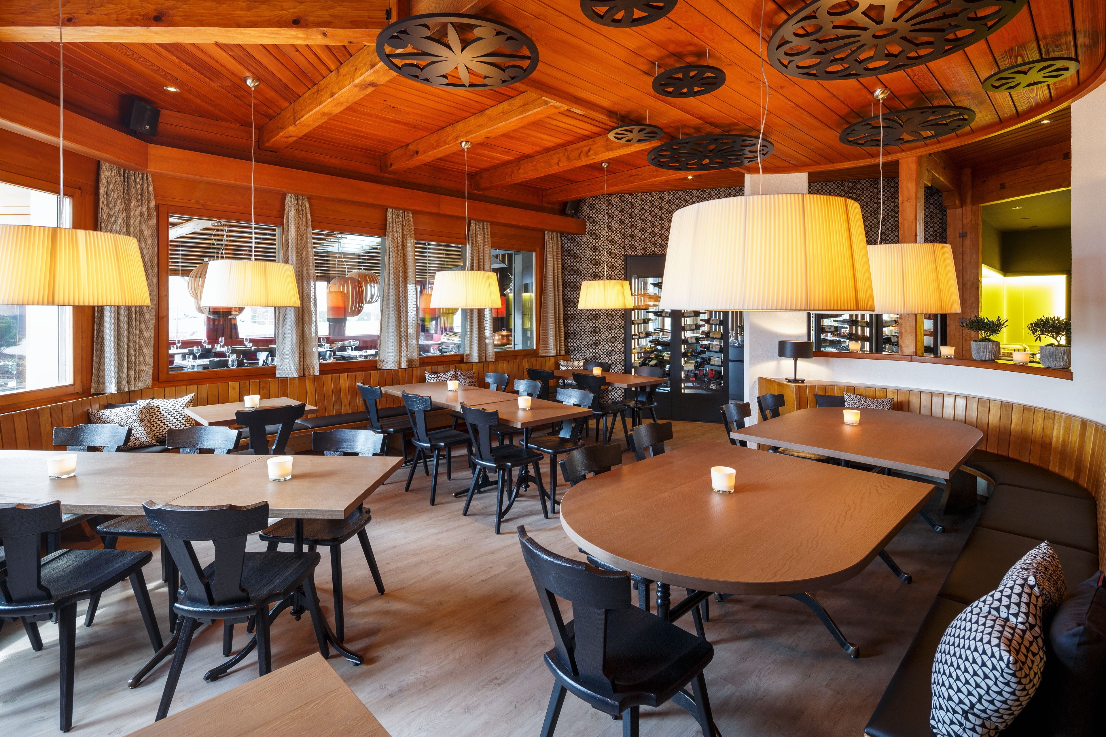 A restaurant with wooden ceiling and walls, multiple tables and chairs, and hanging lamps.