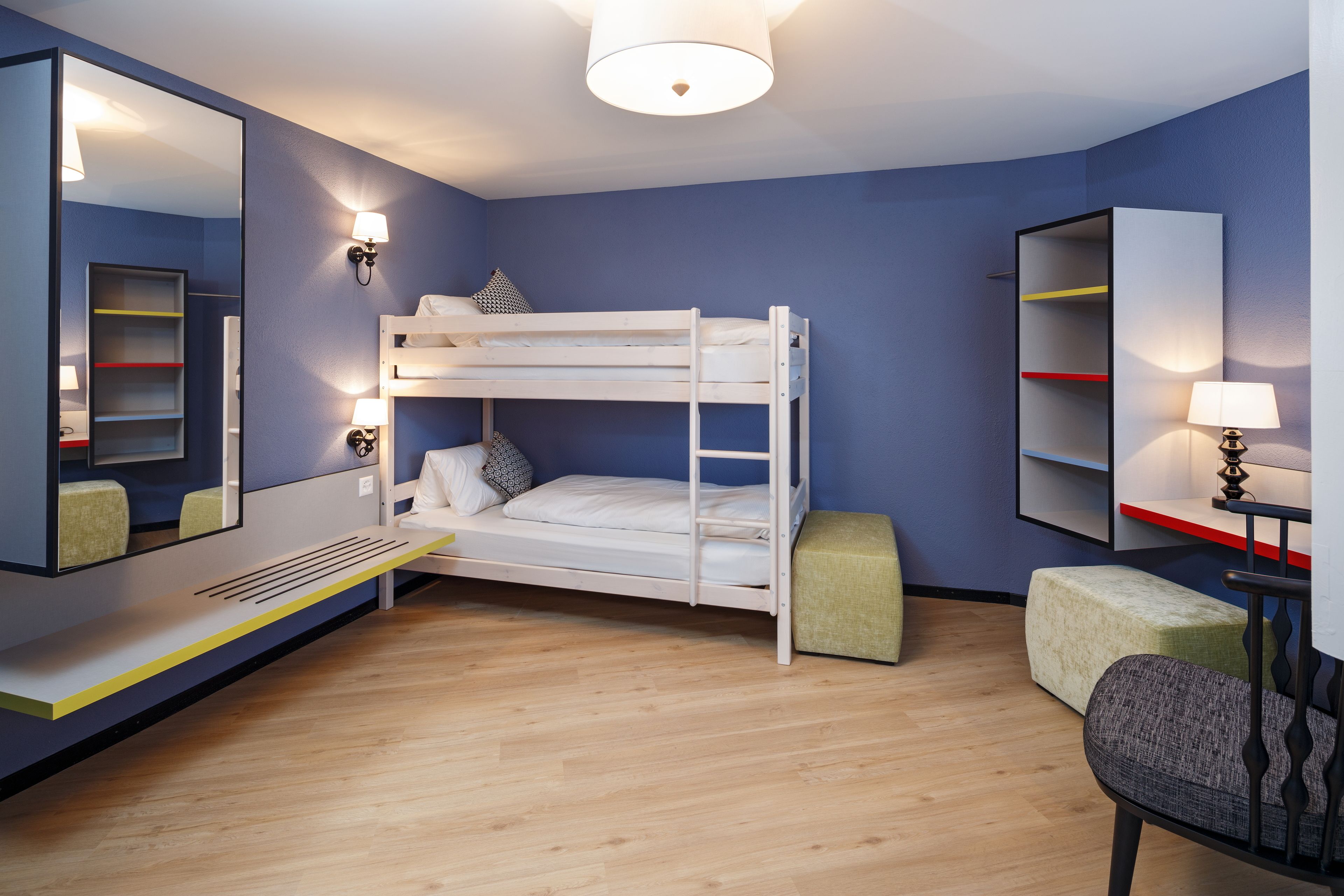 A bunk bed room with a mirror, bedside lamps, and a small desk with a chair.