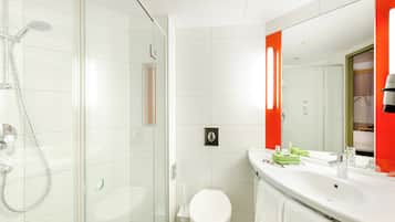 Ein modernes Badezimmer mit Duschkabine aus Glas, einer weißen Toilette und einem Waschtisch mit großem Spiegel und roten Akzenten.