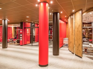 En moderne lobby med røde detaljer, en glas elevator og et siddeområde med en person.