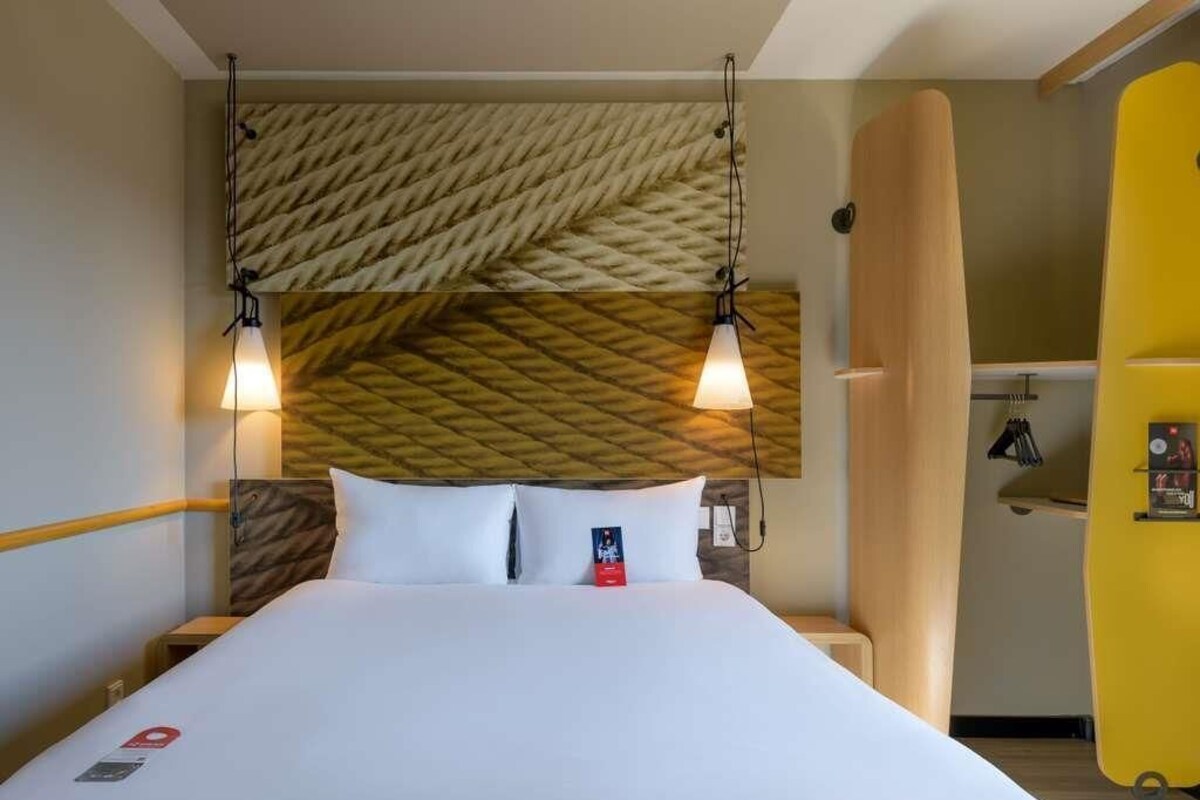 Et hotelværelse med en seng, to sengeborde med lamper, en træsenggavl og en gul væg.