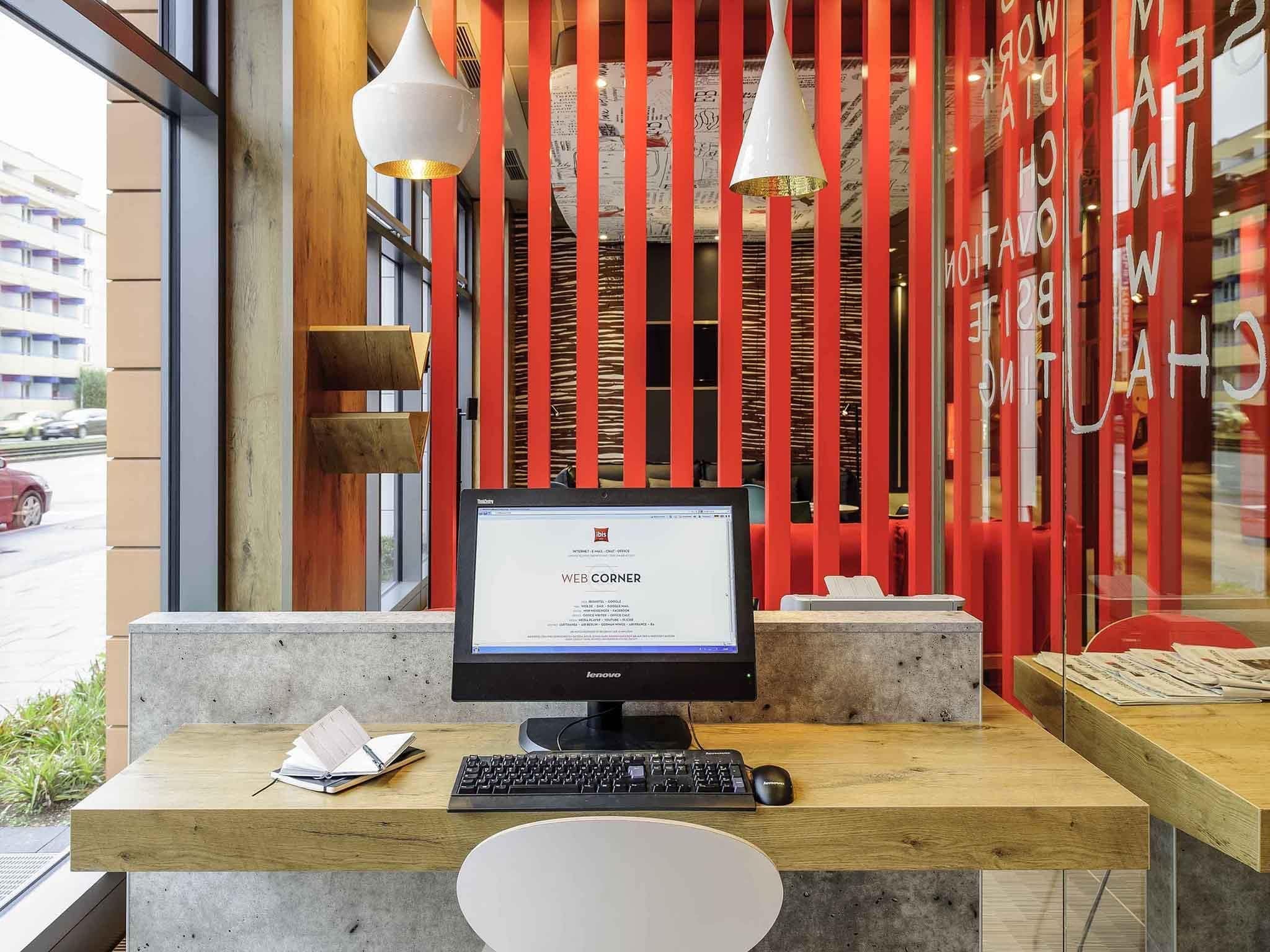 A reception desk with a computer, a keyboard, and a mouse. There is a wooden table and a white chair in front of the desk.