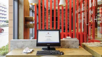 A reception desk with a computer, a keyboard, and a mouse. There is a wooden table and a white chair in front of the desk.