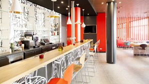 A modern bar area with a long counter, bar stools, and a wall with abstract drawings. - Ibis Muenchen City Arnulfpark (Munich)
