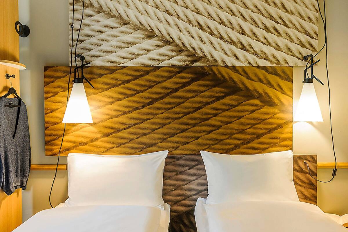 A hotel room with a headboard featuring a textured pattern, two bedside lamps, and a neatly made bed with white linens.