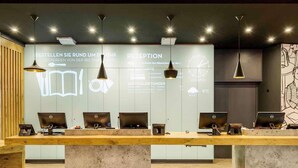 A reception desk with multiple computer stations, a large wall with text and graphics, and pendant lighting. - Ibis Muenchen City Arnulfpark (Munich)